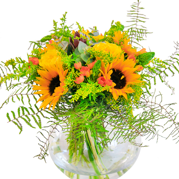 The essence of Bracknell Forest's woodlands and wildflower fields finds new expression in this vibrant floral arrangement. Towering sunflowers, their bright golden petals fanning outward from deep brown centers, lead the composition, reminiscent of sunbeams filtering through ancient trees on a late summer afternoon. Nestled among the sunflowers are lush yellow garden roses, unfurling in soft spirals with a subtle, inviting scent, just like blooms gathered from a local garden in Ascot or Sandhurst. Clusters of bright red Hypericum berries catch flashes of sunlight, sparkling against a rich underlayer of emerald ferns and light sprays of goldenrod, bringing to mind the mosaic of colors woven through Bracknell Forest's natural habitats. Slender stems of eucalyptus, tinted a cool blue-green, peek through the arrangement, infusing a touch of wild freshness and evoking the tranquility of woodland air. Set within a clear, spherical glass vase, the arrangement's stems create elegant lines beneath the surface of fresh water, giving the bouquet a grounded, harmonious presentation. Every detail-from the textural play of soft petals to the playful contrast of berry and foliage-reflects the care and artistry of Flower Delivery Bracknell Forest. This bouquet is an ideal choice for celebrations, heartfelt gifts, or for simply infusing a room with the vitality and richness of the local landscape, connecting nature's beauty directly to your home in Bracknell Forest.